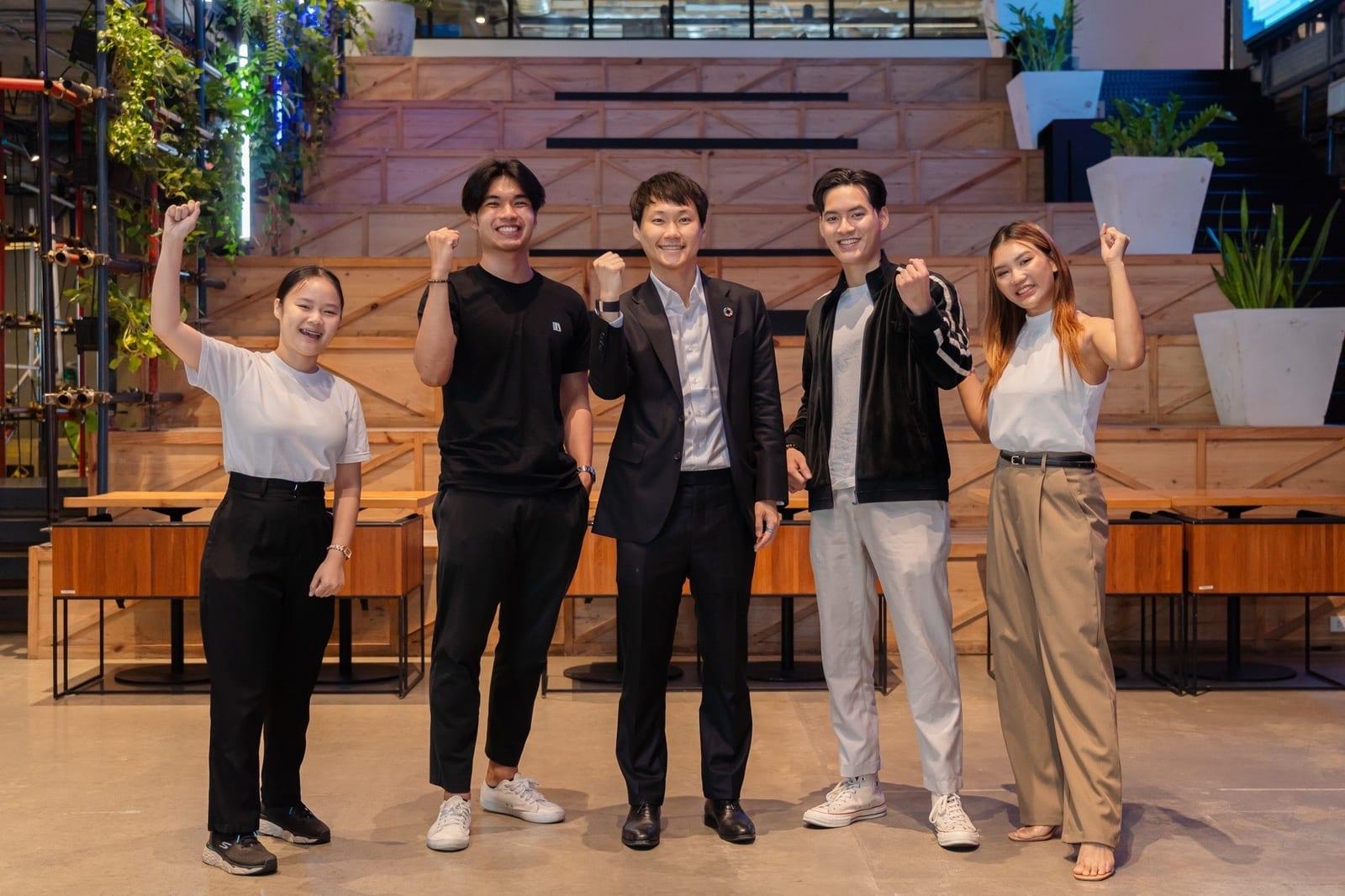 ผมกับอีกสี่คนยืนชูกำปั้นด้วยกันหน้าขั้นบันไดไม้ในพื้นที่ทำงาน